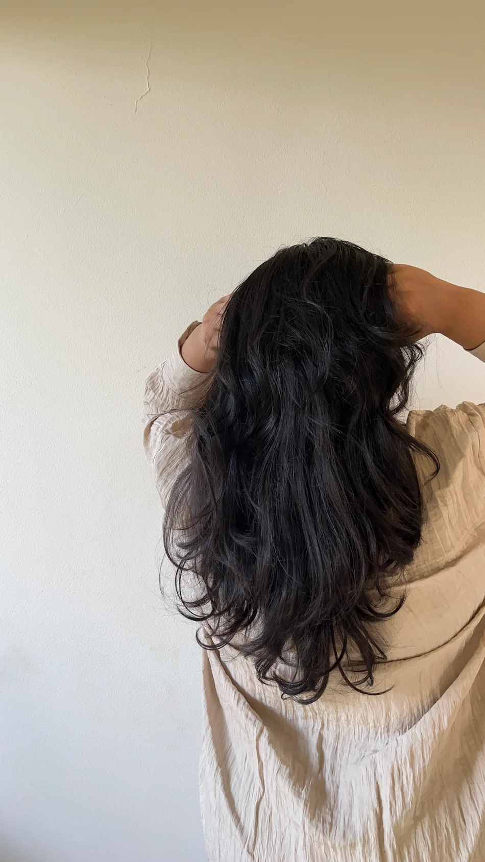 Mulher de costas com as mãos no cabelo escuro, a afastar os fios junto à raiz.
