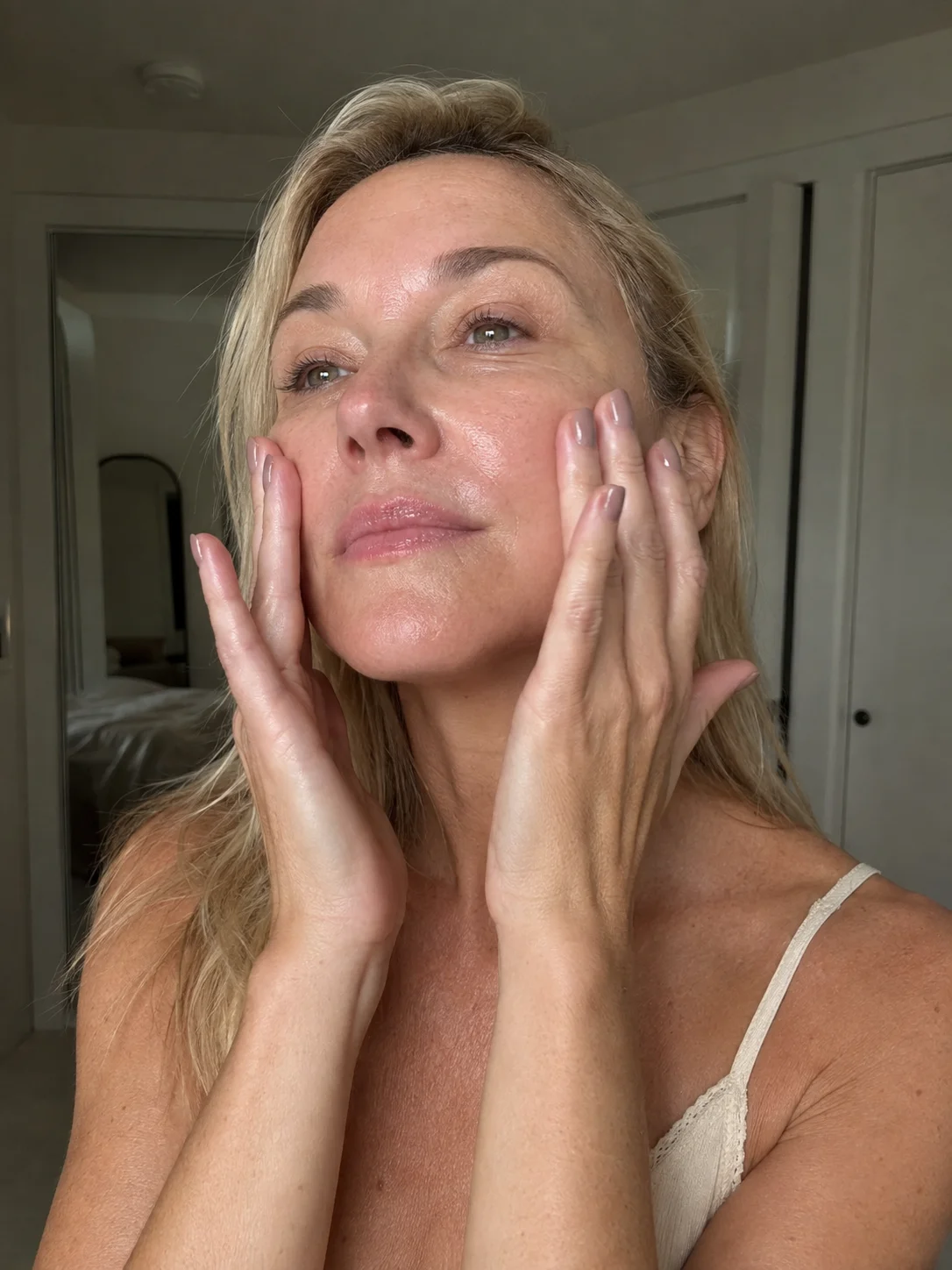 Mulher madura a aplicar hidratante no rosto com pele natural e textura visível