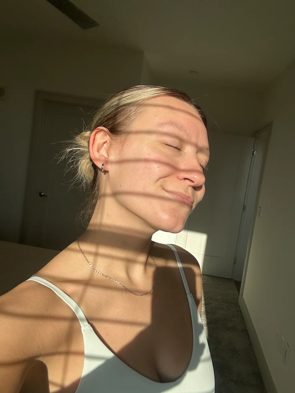Mulher junto a uma janela com luz solar direta no rosto e pele natural visível