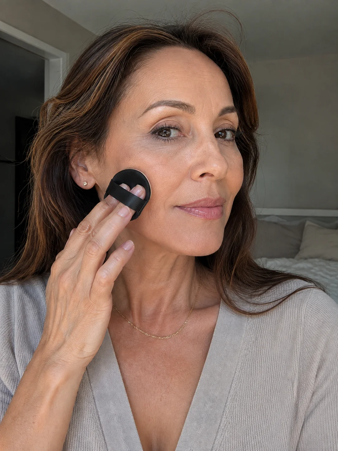 Mulher com pele madura a aplicar base cushion na face com puff de maquilhagem.