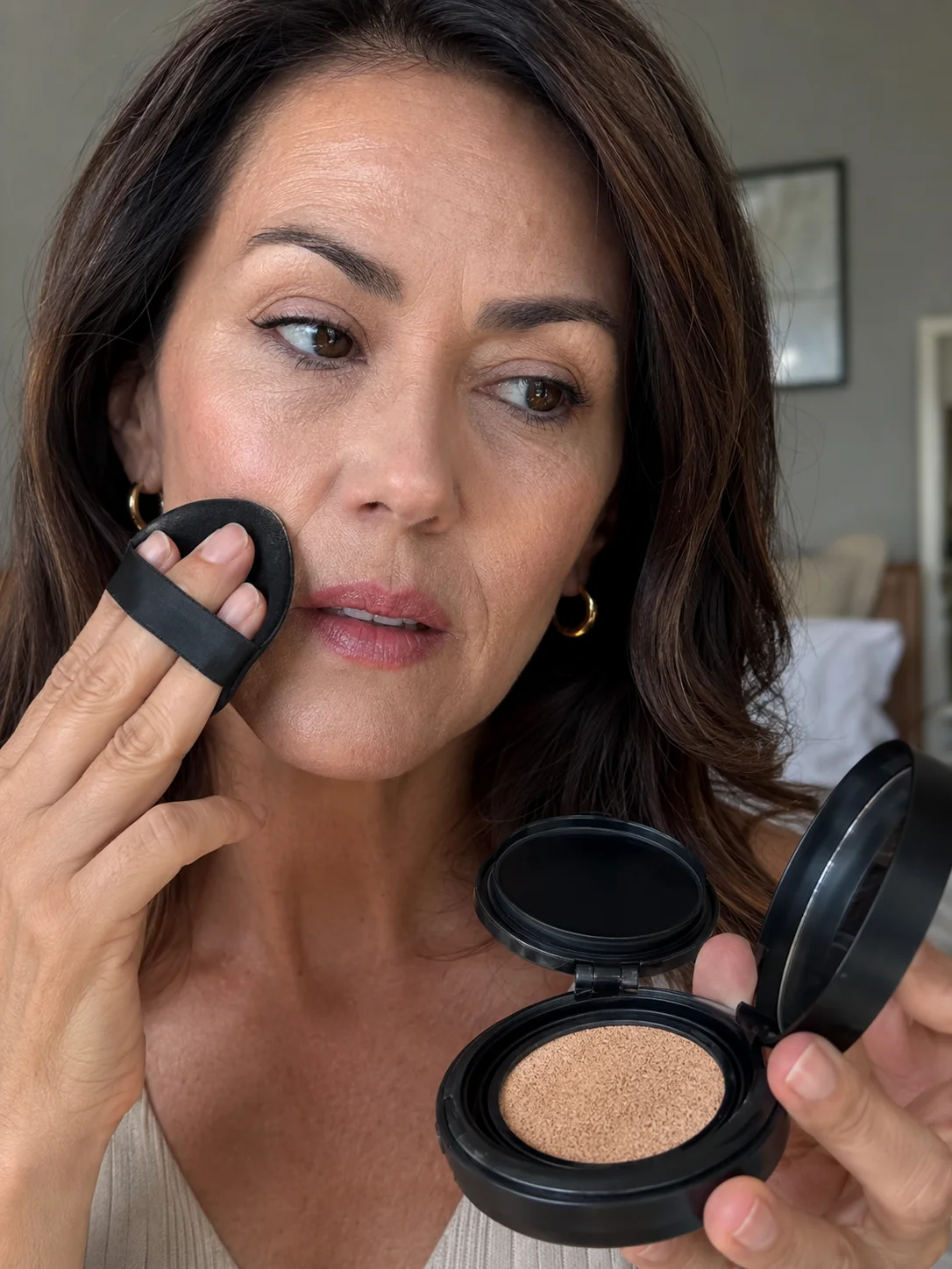Mulher com pele madura a aplicar base cushion no rosto com puff de maquilhagem.