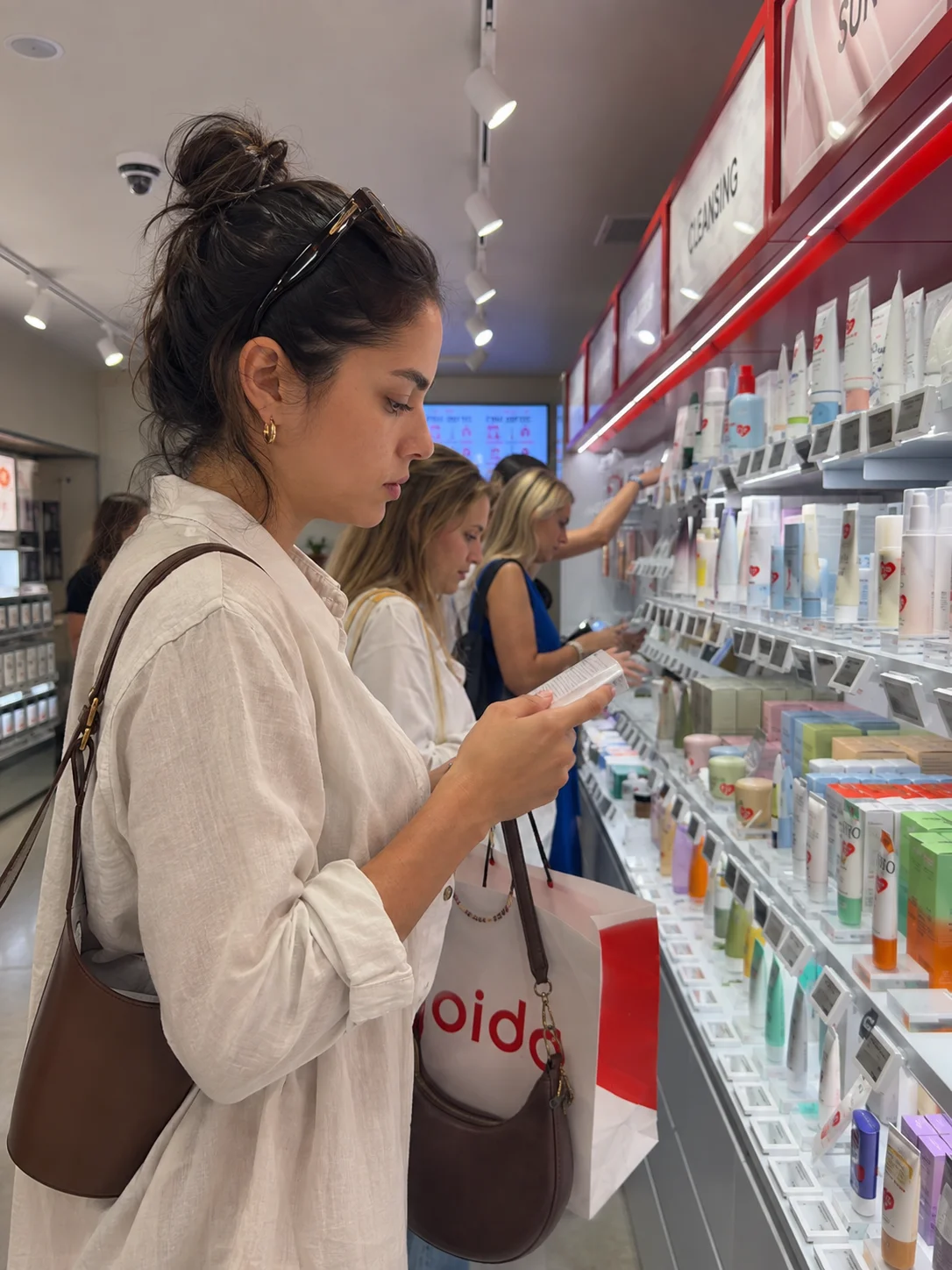 Mulher a ler o rótulo de um produto numa loja MOIDA, junto a prateleiras de cosmética coreana.