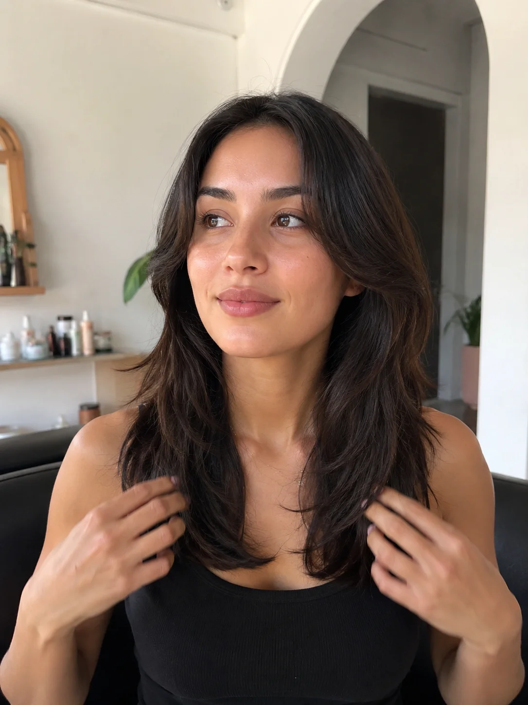 Mulher com cabelo castanho pelos ombros, com volume natural e movimento, junto a um espelho.
