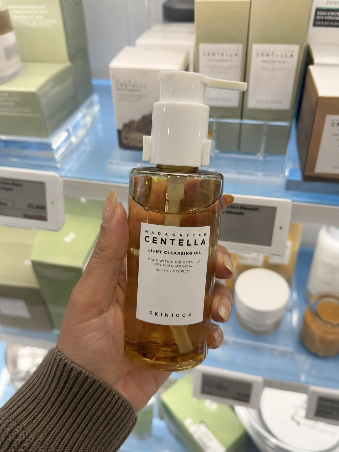 Mão a segurar o óleo de limpeza SKIN1004 Madagascar Centella Light Cleansing Oil numa prateleira de skincare coreana.