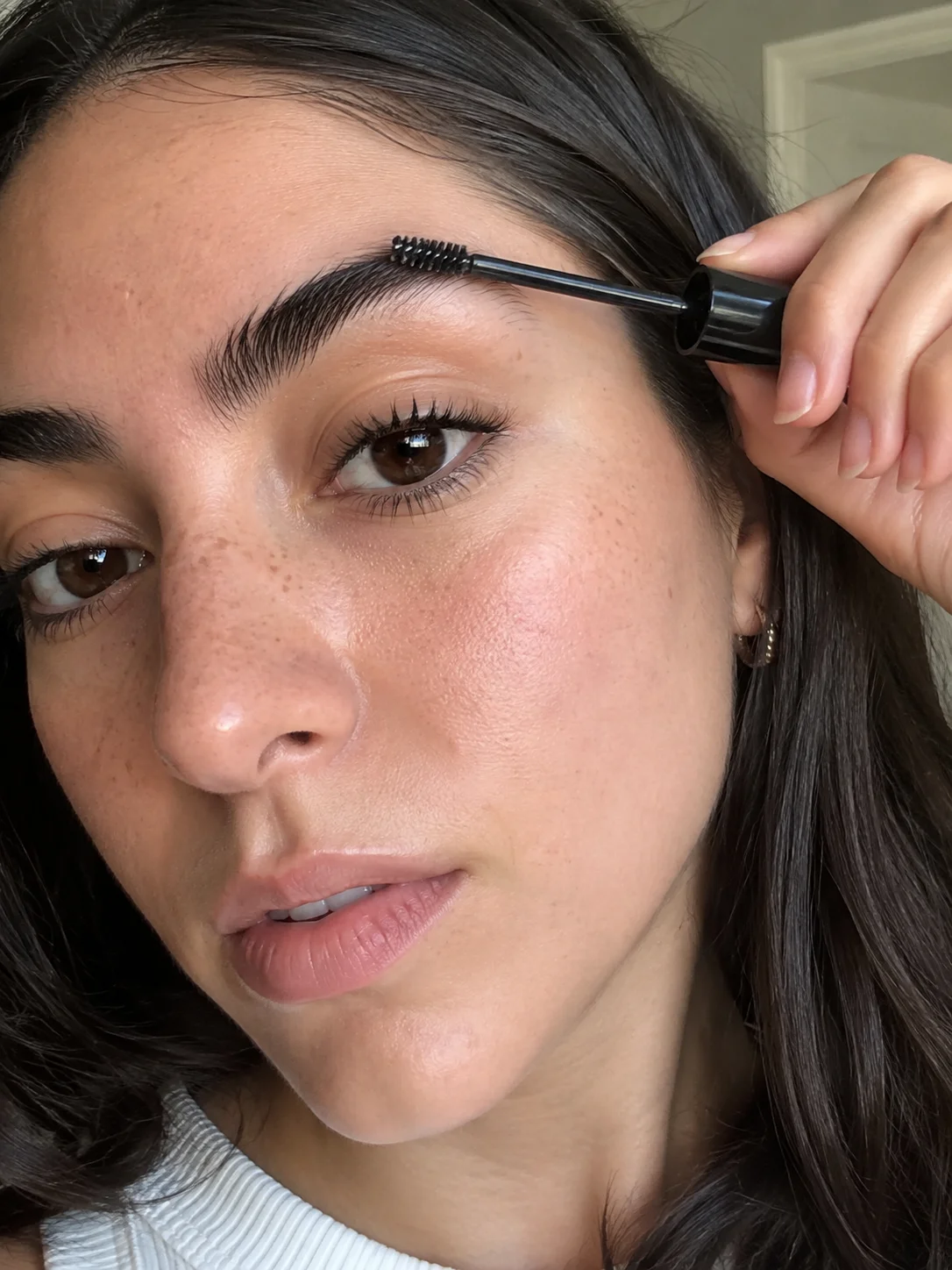 Mulher a pentear as sobrancelhas com maquilhagem natural e pele com textura visível