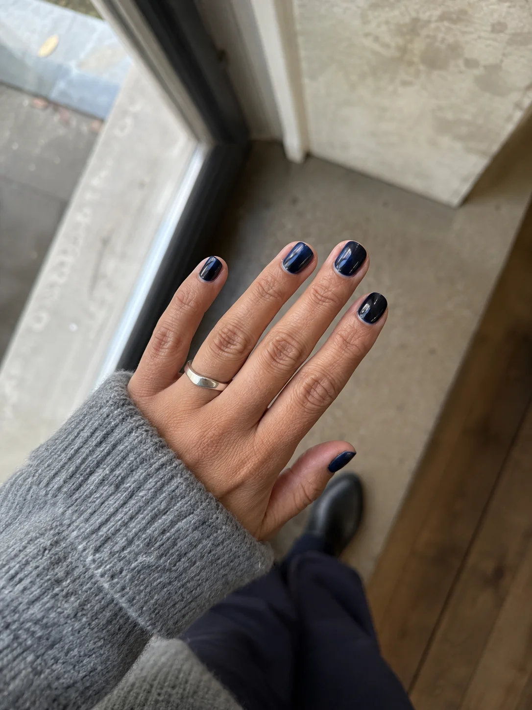 Mão com unhas curtas pintadas em azul meia-noite brilhante junto a uma janela.