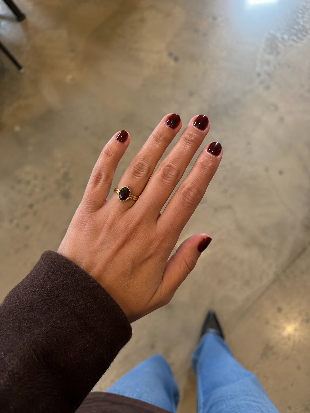 Mão com unhas curtas pintadas em bordô merlot brilhante e anel com pedra escura.