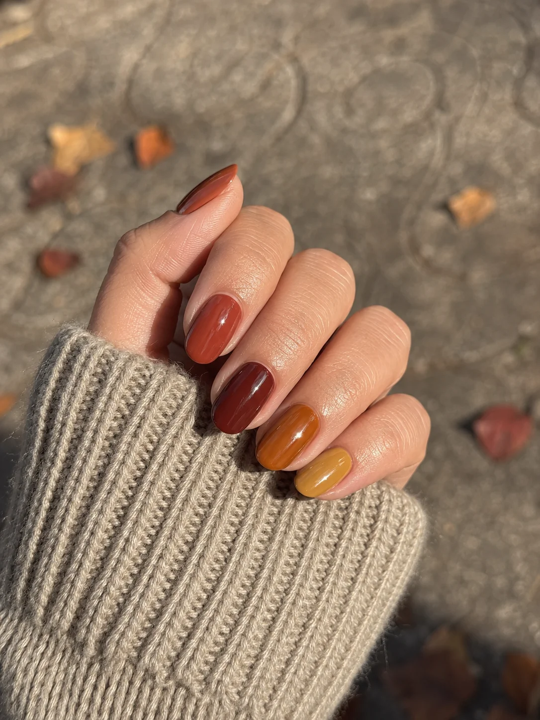Mão com unhas curtas pintadas em tons de terracota, mogno, âmbar e mostarda suave.
