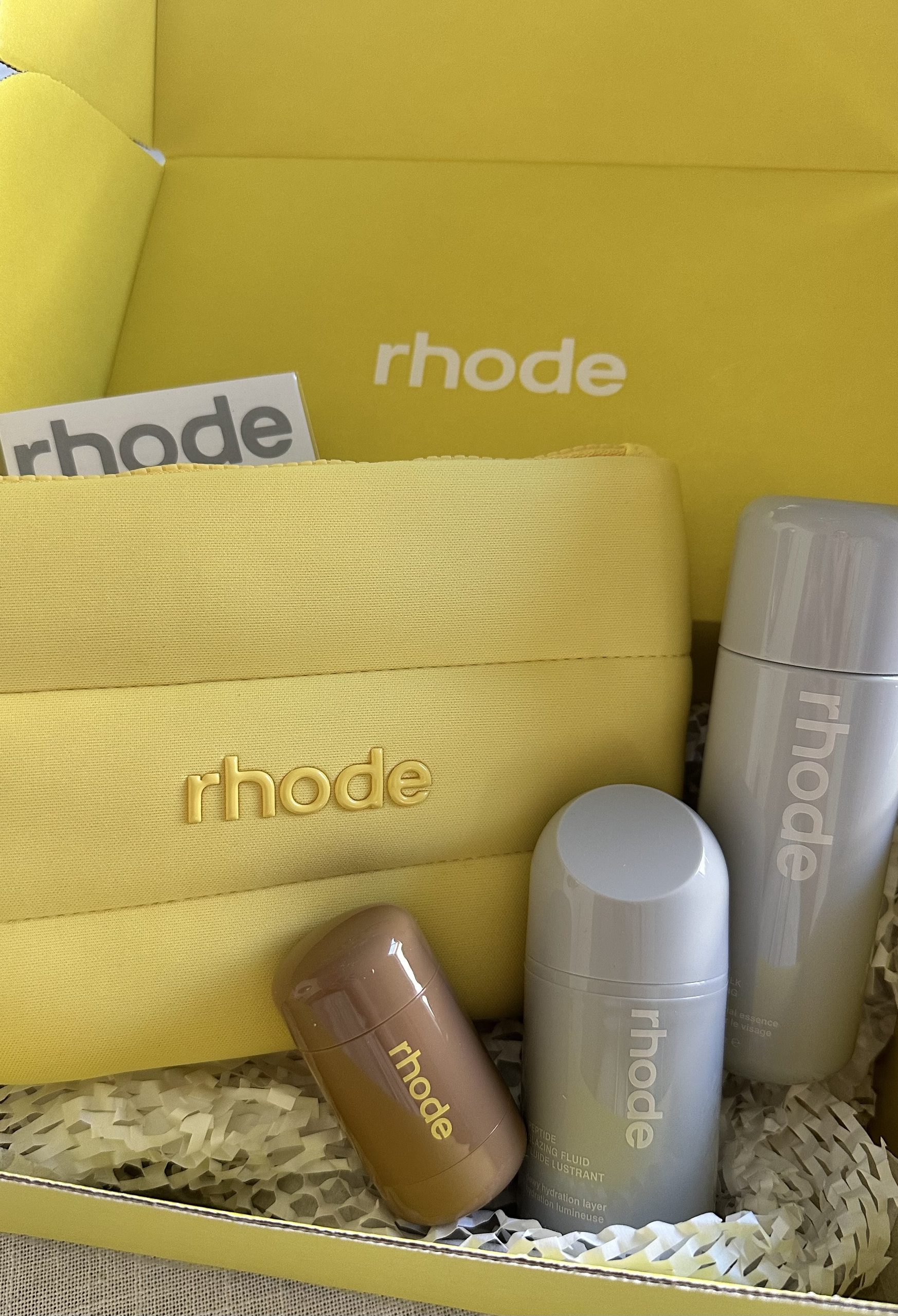 Conjunto de produtos Rhode de skincare e maquilhagem numa caixa amarela com bolsa da marca
